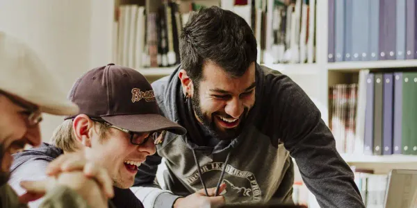 Two smiling men are gathered at a desk in an office.