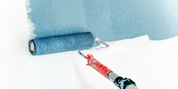 A painting roller is applying blue paint acrss a white wall.